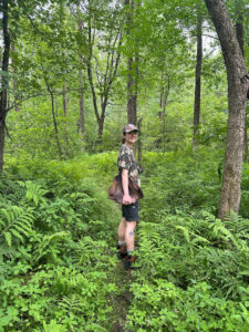 Photo of Theo standing in the woods holding a piece of wood