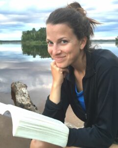 Photo of Kate Seitz reading a book in front of a lake. 