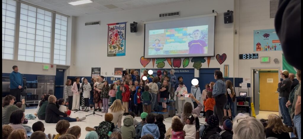 First graders and 5th graders perform together at community meeting.